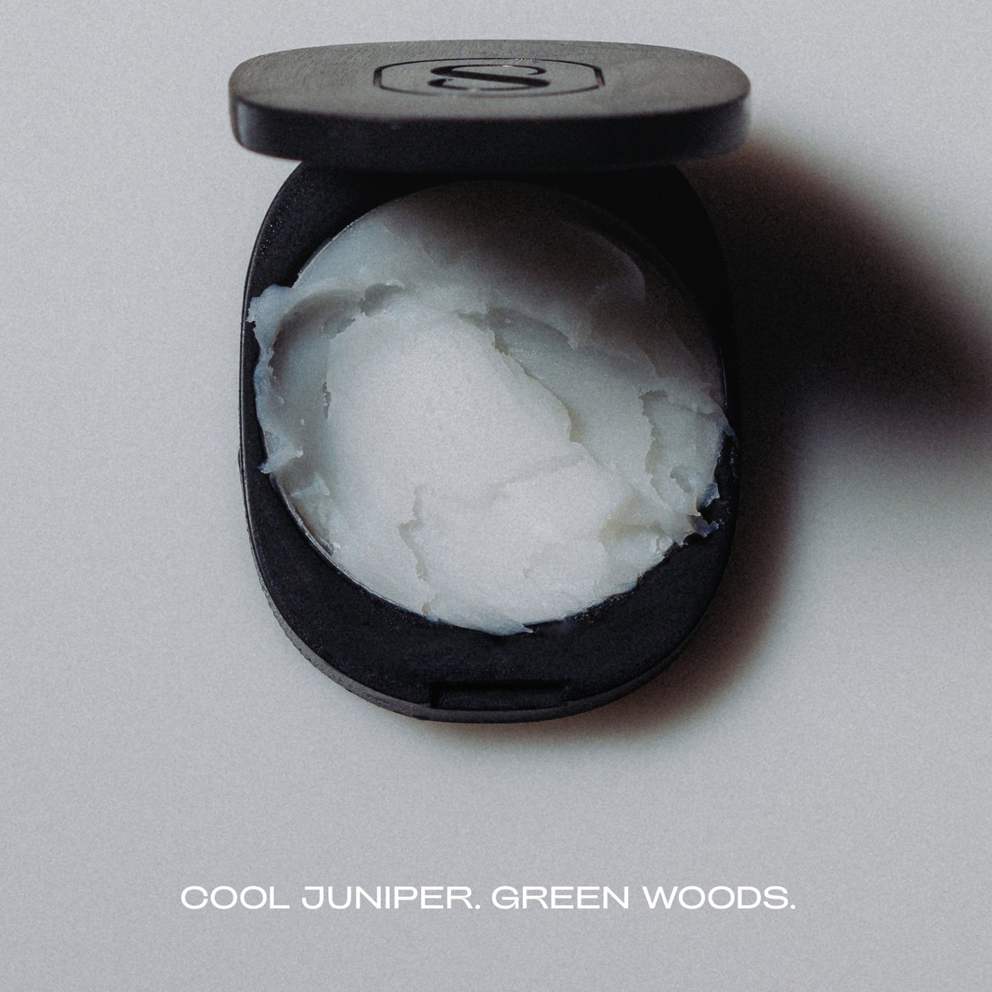 Black container with white substance labeled 'Cool Juniper, Green Woods' on a gray background