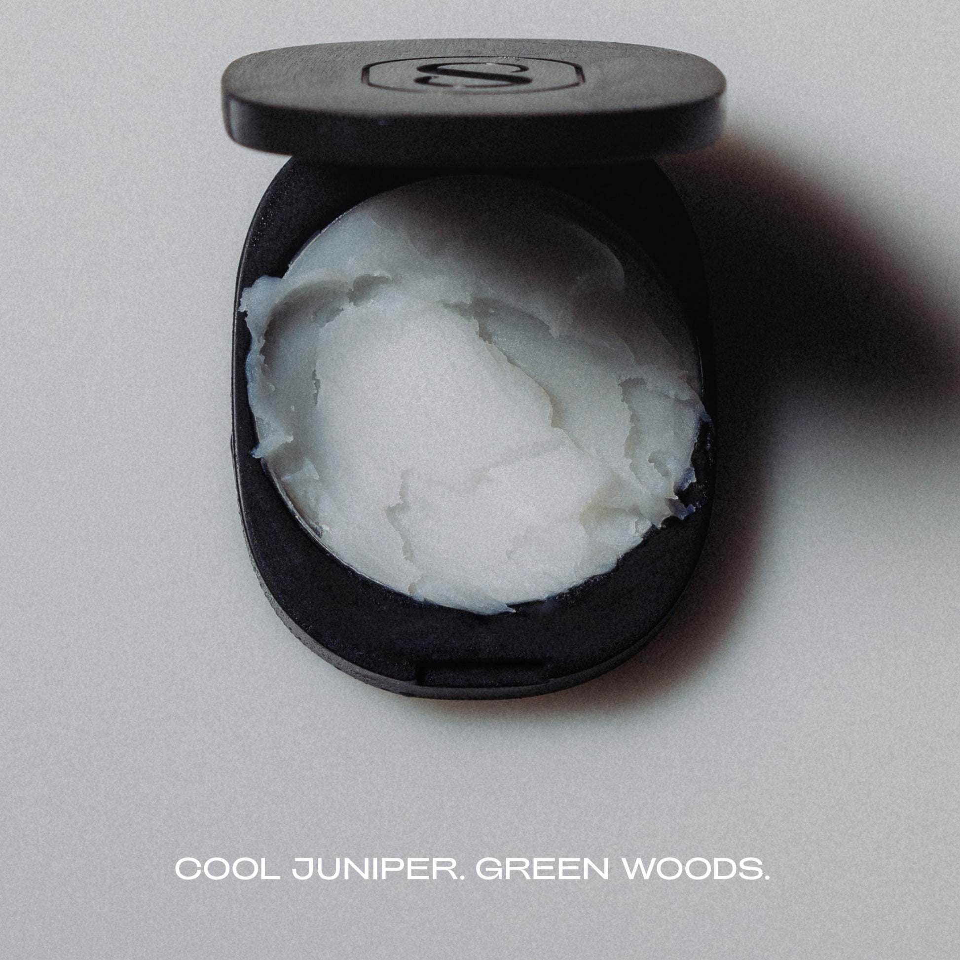 Black container with white substance labeled 'Cool Juniper, Green Woods' on a gray background