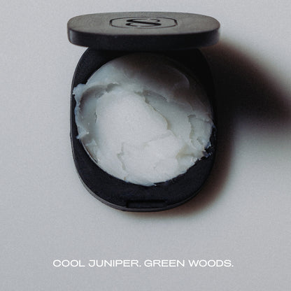 Black container with white substance labeled 'Cool Juniper, Green Woods' on a gray background